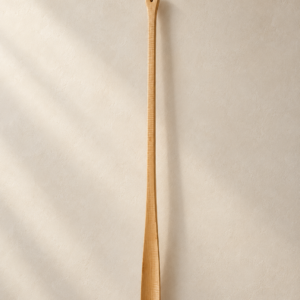 Langer Schuhlöffel aus hellem Holz mit Aufhängeschlaufe vor einer hellen Wand