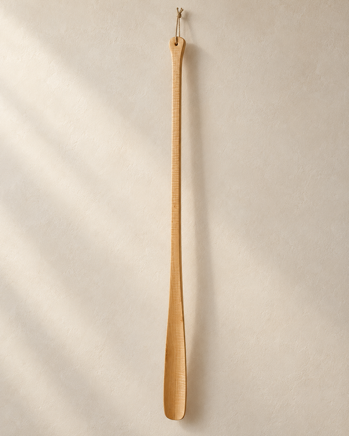 Schuhlöffel aus Holz – Tischlerei Rieger Langer Schuhlöffel aus hellem Holz mit Aufhängeschlaufe vor einer hellen Wand